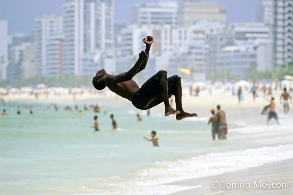 Fotografia di Tonino Mosconi di un ragazzo che fa il salto della morte sulla Spiaggia di Ipanema, a Capoeira, Rio de Janeiro, Brasile